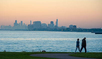 A couple walking along the lake path with Chicago's skyline in the background.